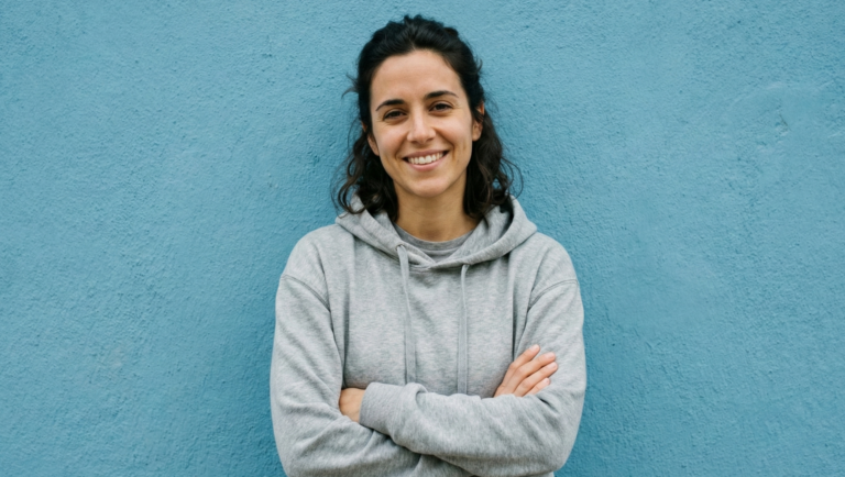 Lächelnde Person in grauem Hoodie vor blauer Wand